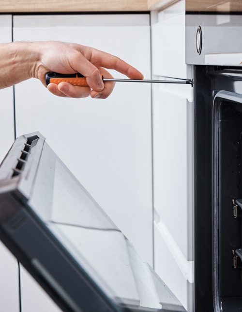 Person using screwdriver to repair an oven door.